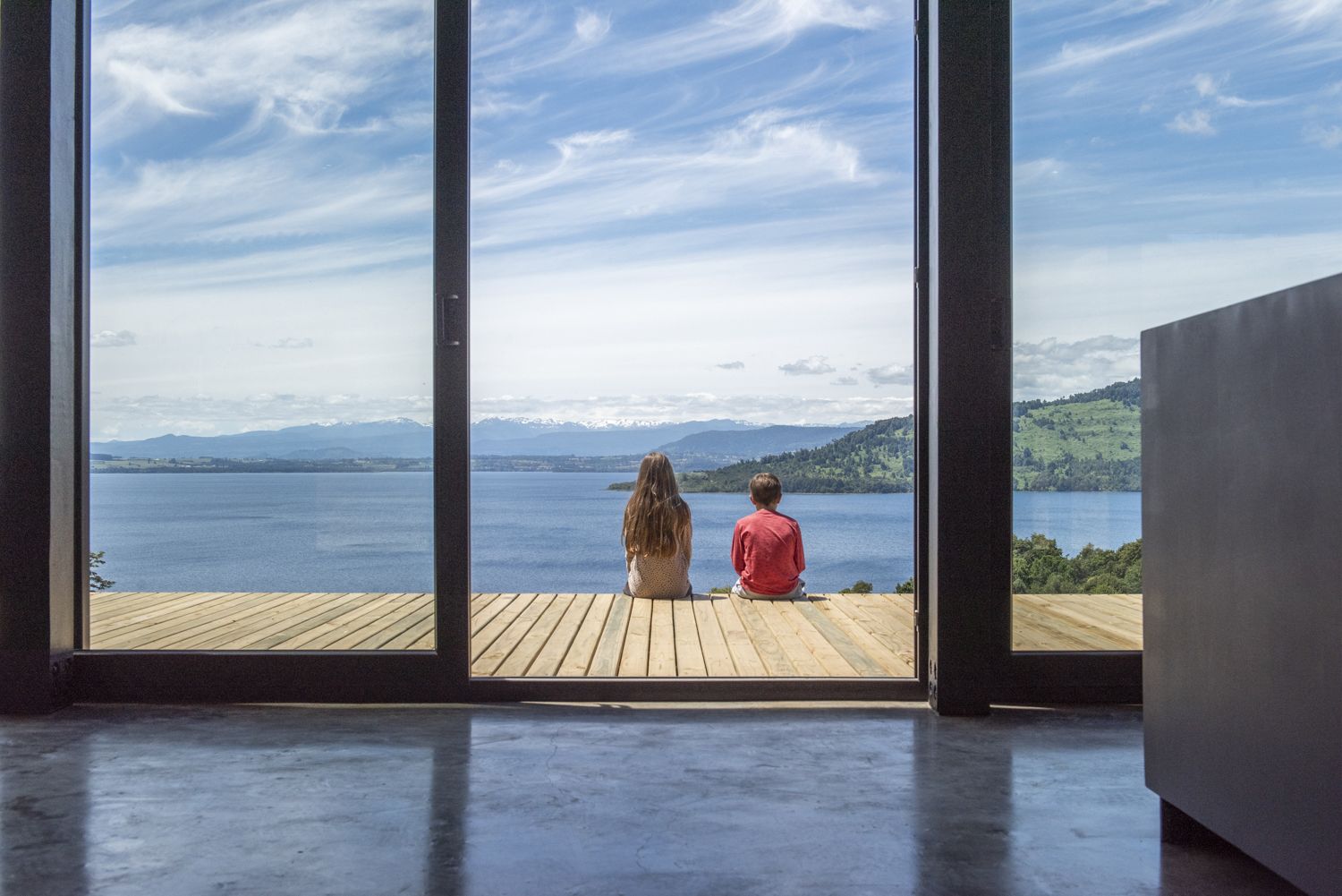 Dos personas sentadas en la terraza frente a un ventanal con vista al lago